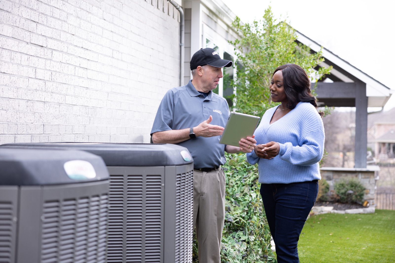 HVAC Maintenance Plan Visit HVAC technician discussing maintenance service with a homeowner beside an outdoor air conditioning unit